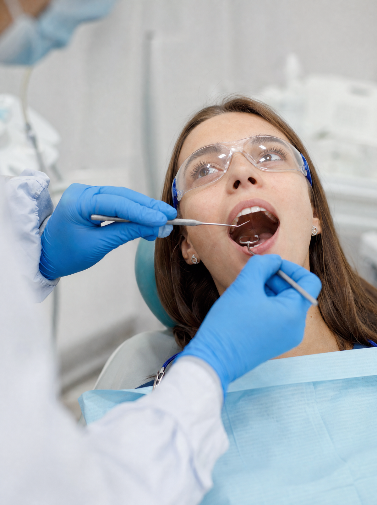 Dentist in blue nitrile gloves examining a patient with a mirror and probe