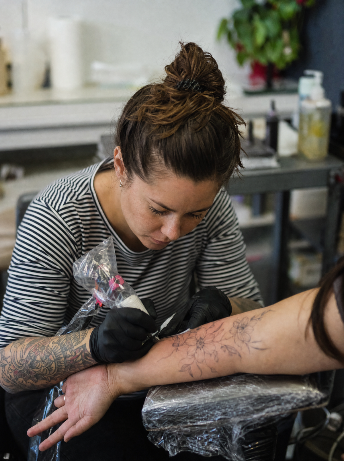 Tattoo artist in black nitrile gloves working a fine-line forearm tattoo
